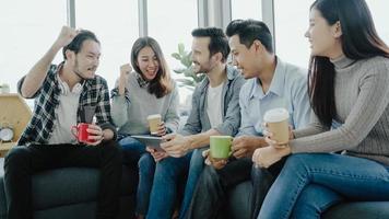 Multiethnic creative team diversity of young people group team holding coffee cups and discussing ideas meeting with tablet sitting on the couch at office. Coffee break time at creative office. photo