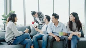 Diversity of young people group team holding coffee cups and discussing something with smile while sitting on the couch at office. Coffee break time at creative office. photo