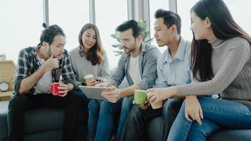 Multiethnic creative team diversity of young people group team holding coffee cups and discussing ideas meeting with tablet sitting on the couch at office. Coffee break time at creative office. photo