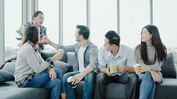 diversidad del equipo del grupo de jóvenes sosteniendo tazas de café y discutiendo algo con una sonrisa mientras está sentado en el sofá de la oficina. tiempo de descanso para tomar café en la oficina creativa. foto