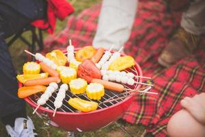 Group of man and woman enjoy camping picnic and barbecue at lake with tents in background. Young mixed race Asian woman and man. Vintage effect style pictures. photo