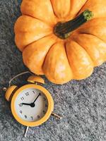 Ripe orange pumpkin and yellow alarm clock on gray, top view. Daylight savings time concept. photo