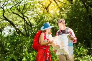 Hiking - hikers looking at map. Couple or friends navigating together smiling happy during camping travel hike outdoors in forest. Young mixed race Asian woman and man. photo