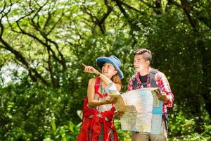 Hiking - hikers looking at map. Couple or friends navigating together smiling happy during camping travel hike outdoors in forest. Young mixed race Asian woman and man. photo