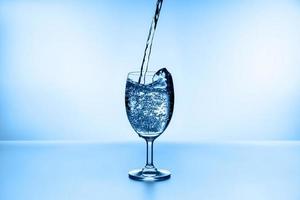 Pouring water into glass on blue background photo