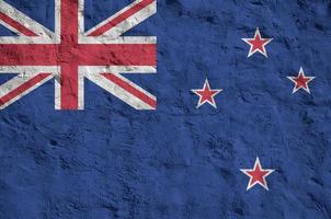 New Zealand flag depicted in bright paint colors on old relief plastering wall. Textured banner on rough background photo