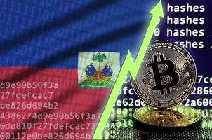 bandera de haití y flecha verde ascendente en la pantalla de minería bitcoin y dos bitcoins dorados físicos foto