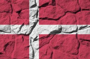Denmark flag depicted in paint colors on old stone wall closeup. Textured banner on rock wall background photo