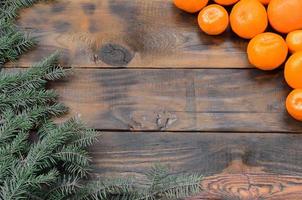 A lot of orange mandarins and Christmas fir branches are lying on a brown wooden planks photo