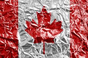 Canada flag depicted in paint colors on shiny crumpled aluminium foil closeup. Textured banner on rough background photo