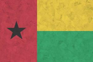Guinea Bissau flag depicted in bright paint colors on old relief plastering wall. Textured banner on rough background photo