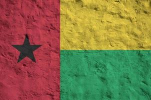 Guinea Bissau flag depicted in bright paint colors on old relief plastering wall. Textured banner on rough background photo