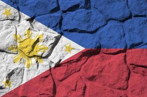 Philippines flag depicted in paint colors on old stone wall closeup. Textured banner on rock wall background photo