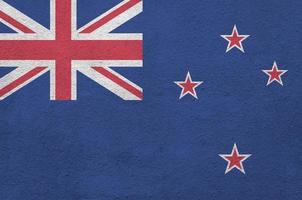 New Zealand flag depicted in bright paint colors on old relief plastering wall. Textured banner on rough background photo