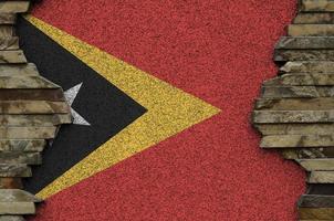 Timor Leste flag depicted in paint colors on old stone wall closeup. Textured banner on rock wall background photo