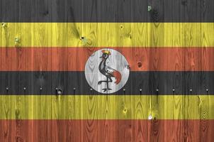 Uganda flag depicted in bright paint colors on old wooden wall. Textured banner on rough background photo