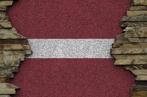 Latvia flag depicted in paint colors on old stone wall closeup. Textured banner on rock wall background photo