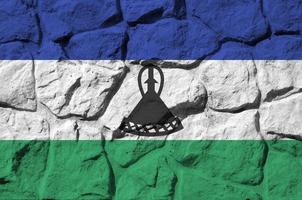 Lesotho flag depicted in paint colors on old stone wall closeup. Textured banner on rock wall background photo