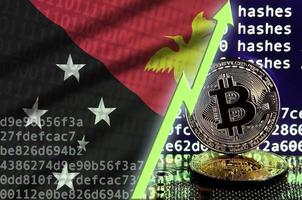 bandera de papúa nueva guinea y flecha verde ascendente en la pantalla de minería bitcoin y dos bitcoins dorados físicos foto