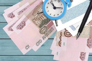 100 russian rubles bills and alarm clock with pen and envelopes. Tax season concept, payment deadline for credit or loan. Financial operations using postal service photo