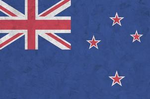 New Zealand flag depicted in bright paint colors on old relief plastering wall. Textured banner on rough background photo