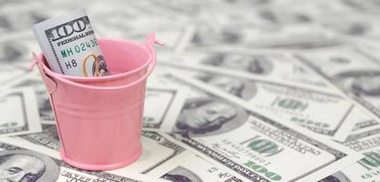 A bundle of US dollars in a metal pink bucket on a set of dollar bills photo