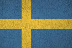 Sweden flag depicted in bright paint colors on old relief plastering wall. Textured banner on rough background photo