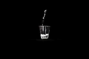 un vaso de agua con un chorro de agua que cae sobre un fondo negro infinito foto