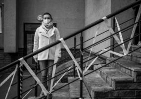 Photo of a girl in a mask. Standing on the street with danger warning tapes.