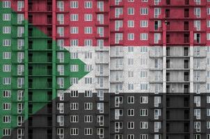 Sudan flag depicted in paint colors on multi-storey residental building under construction. Textured banner on brick wall background photo