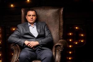 handsome businessman in a suit looks at the camera on a leather chair. photo