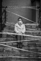 Photo of a girl in a mask. Sitting on the street with danger warning tapes.