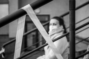 Photo of a girl in a mask. Sitting on the street with danger warning tapes.