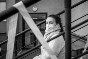 Photo of a girl in a mask. Sitting on the street with danger warning tapes.