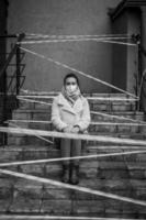 Photo of a girl in a mask. Sitting on the street with danger warning tapes.