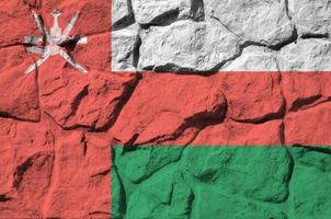 Oman flag depicted in paint colors on old stone wall closeup. Textured banner on rock wall background photo