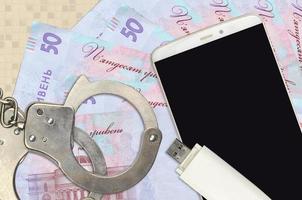 50 Ukrainian hryvnias bills and smartphone with police handcuffs. Concept of hackers phishing attacks, illegal scam or malware soft distribution photo