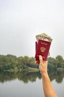 un pasaporte extranjero y dólares en la mano, en el contexto de la naturaleza. foto