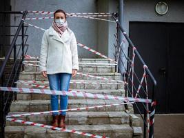 Photo of a girl in a mask. Standing on the street with danger warning tapes.