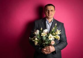 un apuesto hombre de negocios con traje mira a la cámara con un ramo de flores. foto