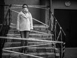 Photo of a girl in a mask. Standing on the street with danger warning tapes.