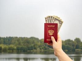 un pasaporte extranjero y dólares en la mano, en el contexto de la naturaleza. foto