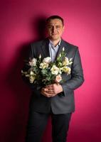 handsome businessman in a suit looks at the camera with a bouquet of flowers. photo