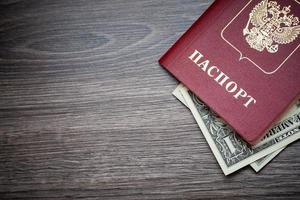 un pasaporte extranjero y dólares sobre un fondo de madera. foto