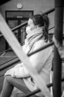 Photo of a girl in a mask. Sitting on the street with danger warning tapes.