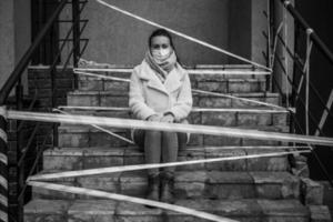 Photo of a girl in a mask. Sitting on the street with danger warning tapes.