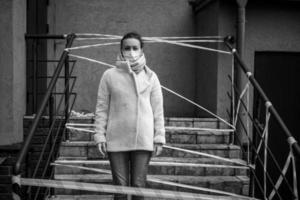 Photo of a girl in a mask. Standing on the street with danger warning tapes.