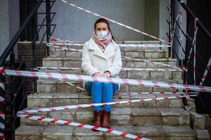 Photo of a girl in a mask. Sitting on the street with danger warning tapes.