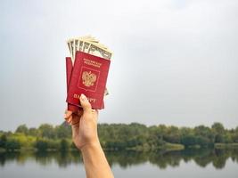 un pasaporte extranjero y dólares en la mano, en el contexto de la naturaleza. foto