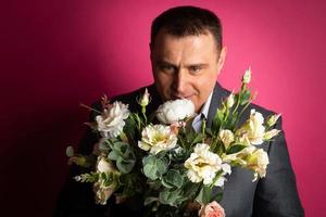 un apuesto hombre de negocios con traje mira a la cámara con un ramo de flores. foto